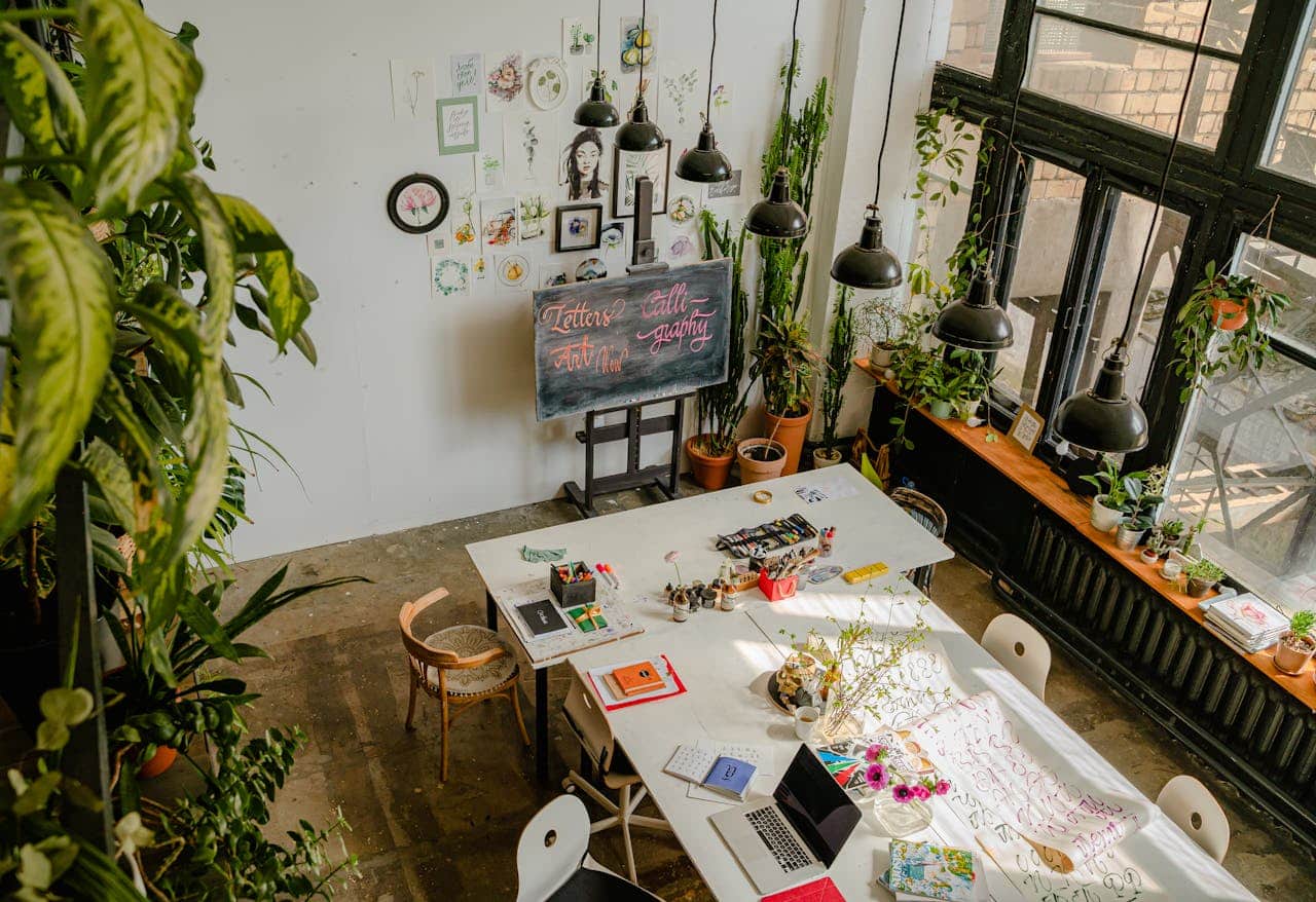Bright creative workspace featuring calligraphy tools, potted plants, and a white table setup.